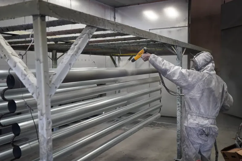 Worker powder-coating a pipe indoors